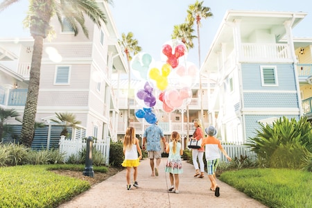 A family holding Mickey Mouse balloons while walking down a sunny path at Disney's Old Key West Resort