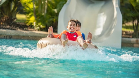 Two kids ride a float off of a water slide into a pool of water
