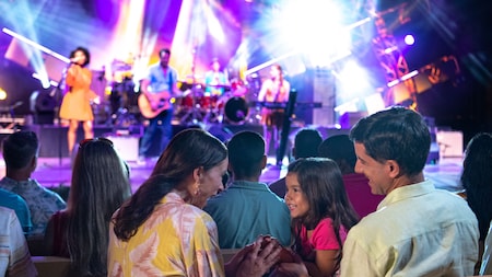 A family of 3 smiling at one another as they watch a concert at America Gardens Theatre at EPCOT