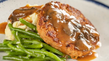 A slice of meatloaf, mashed potatoes with gravy and string beans on a plate
