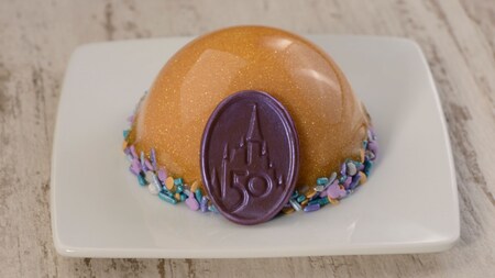 Uma sobremesa de cheesecake de framboesa em forma de domo com um medalhão de chocolate do 50.º aniversário