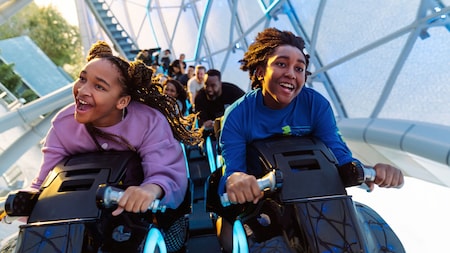 Guests smile while holding on to ride vehicles at TRON Lightcycle Run