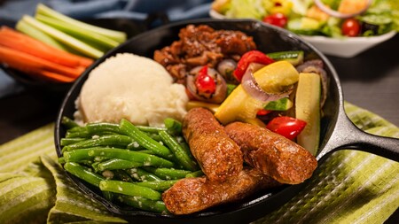 A plate of plant based sausage with mashed potatoes, green beans and roasted vegetables in a skillet