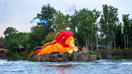 Three kites, including one that looks like Simba and another that looks like Zazu, float over a body of water at Disney’s Animal Kingdom theme park