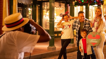 A Disney PhotoPass photographer takes a picture of a family holding a sign that says ‘Happy Holidays’