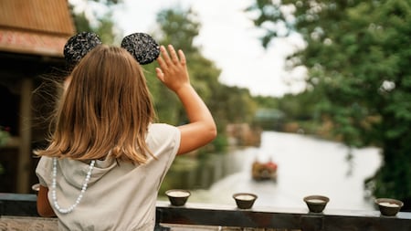 A little girl wearing mouse ears on a bridge waving at a boat at Disney's Animal Kingdom theme park