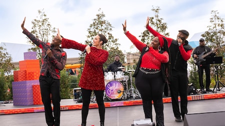 Four performers in holiday outfits singing and dancing on an outdoor stage during the Joyful! A Celebration of the Season show at Epcot