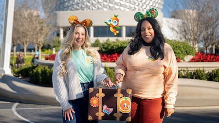 A Disney PhotoPass Magic Shot featuring 2 Guests posing with Orange Bird in front of Spaceship Earth at Epcot