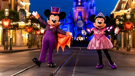 Mickey Mouse dressed like a vampire and Minnie Mouse dressed like a fairy princess, standing near Cinderella Castle at night