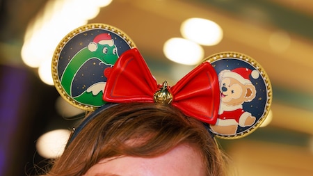 A woman wearing a Minnie Mouse ear headband featuring artwork of Gertie and Ollie.