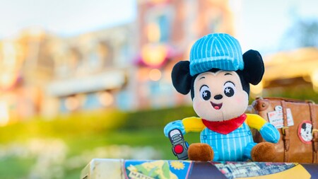 A Wishable Mickey Mouse plush doll, dressed as a train conductor, sitting posed in front of the Disneyland Railroad