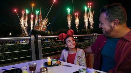 A father and daughter dining together with Cinderella Castle and fireworks behind them