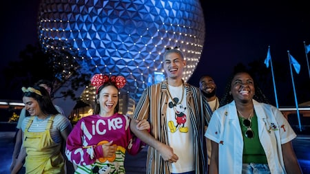 A group of friends walking arm in arm in Epcot with Spaceship Earth illuminated in the background