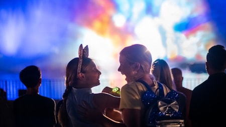 Two friends, one in a Minnie Mouse ear headband, excitedly watch a nighttime spectacular at Disney’s Hollywood Studios in Florida