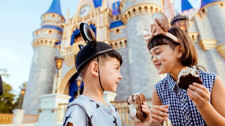 Un niño y una niña comen sándwiches de helado premium de Mickey frente a Cinderella Castle en Magic Kingdom Park