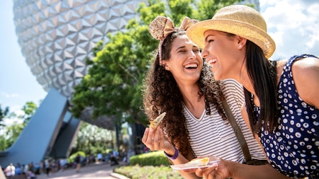 Two women smiling while enjoying a snack near Spaceship Earth at Epcot