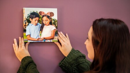 A woman hanging up a canvas print of 2 children posing with a Magic Shot overlay of Tinker Bell