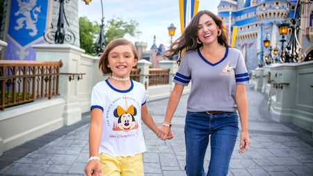 A woman and her daughter holding hands while walking along a bridge at Cinderella Castle in Magic Kingdom park