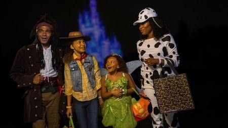 A father, mother and their 2 daughters dressed in Halloween costumes near Cinderella Castle at night