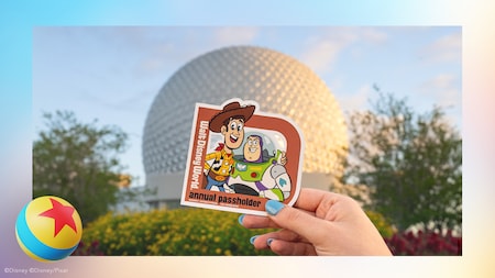 A hand holding an Annual Passholder magnet with Woody and Buzz Lightyear near Spaceship Earth 