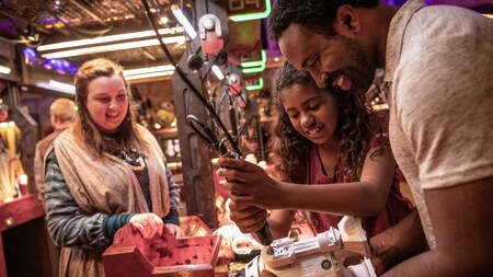 A father and daughter constructing a droid as a Cast Member watches at Droid Depot