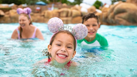 A girl wearing a Minnie Mouse ear headband while swimming in Melt Away Bay at Disney's Blizzard Beach water park