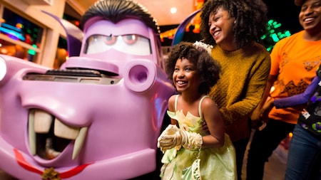 A young girl dressed as Tiana and her family posing next to vampire Mater at Cars Land