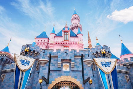 A daytime view of Sleeping Beauty Castle at Disneyland, featuring pink and blue turrets and stone details under a clear blue sky.