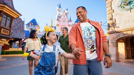 A father and daughter holding hands while walking with their family through Disneyland Park