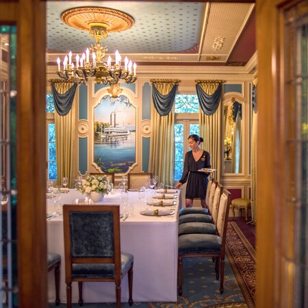 A Cast Member sets a table in a private dining room at 21 Royal in Disneyland Park