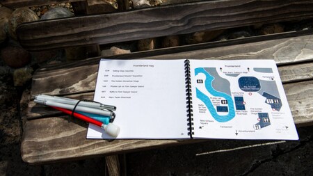 El mapa táctil portátil está abierto en Frontierland sobre un banco junto a un bastón blanco plegable