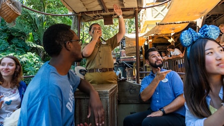 A male Sign Language interpreter narrates the Jungle Cruise on a boat, while a man wearing a hearing aid looks on.