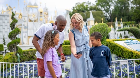 A family of 4 looking at a phone in front of the "it's a small world" attraction at Disneyland