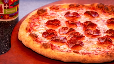 A pepperoni pizza sitting on a tray next to a cup from Alien Pizza Planet at Disneyland Park