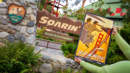 A person holding a poster for Soarin’ Over California in front of the attraction signage