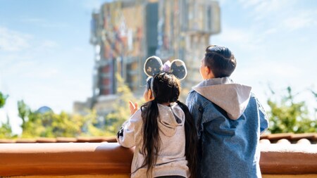 A girl wearing a Minnie Mouse ear headband next to a boy, both admiring the Guardians of the Galaxy Mission Breakout tower