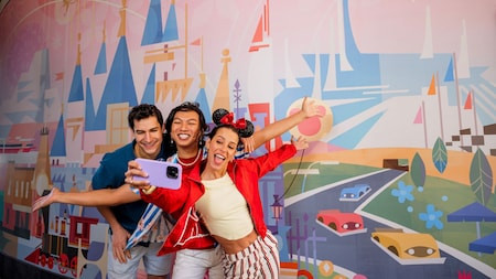 Three Guests taking a selfie in front of a mural of Disneyland Park