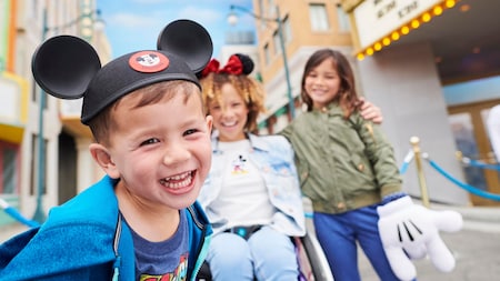 Un niño sonriente con orejas de Mickey Mouse posa con sus 2 hermanas 