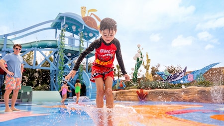 A child jumps and plays on an outdoor water splash pad at Pixar Place Hotel