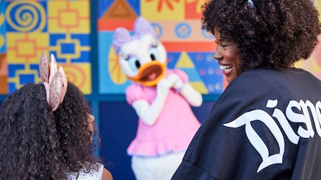 A mother and daughter smile at one another as they approach Daisy Duck