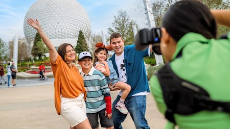 A Disney Photopass photographer taking a picture of a family of 4 in front of Spaceship Earth at Epcot
