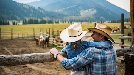 父の背中に腕を回しながら、モンタナの牧場で馬を眺める女の子