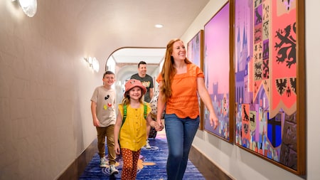 2 人の子供たちとホテルの廊下を歩きながら、壁に飾られたアート作品を鑑賞するカップル