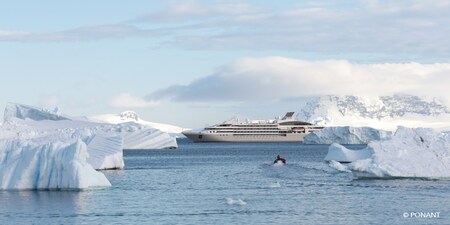 A small boat cruises through ice floe filled waters towards an expedition cruise ship