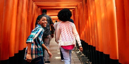 A smiling teen boy looks back as he walks through a long row of torii gates at Fushimi Inari Shrine in Kyoto, Japan