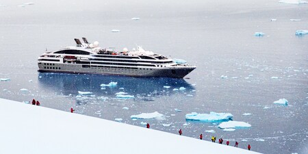 A group of people climb a snowy hill near a cruise ship anchored in the sea amid ice floes