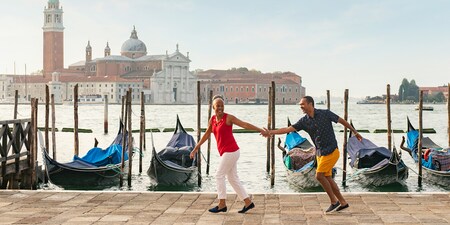 A couple holds hands as they stroll past docked gondolas along the Venice Grand Canal