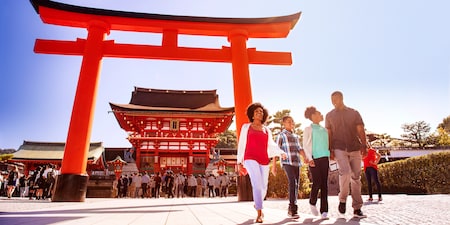 A family of four walks past a Tori gate near the entrance to a Japanese temple