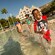 A smiling boy splashes through knee high water with his family watching in the background