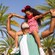 A little girl sits on her father's shoulders in an outdoor setting with palm trees